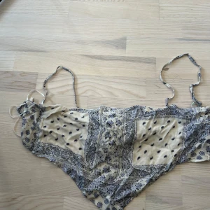 Blommig topp från Pull&Bear - Säljer en ljusblå och vit topp från Pull&Bear med blommigt mönster och knyt i ryggen. Toppen har tunna axelband som är avtagbara och är perfekt för sommaren. Materialet är mjukt och bekvämt, tillverkat i polyester.