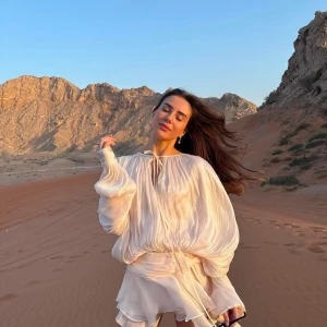 Ljusbeige omlottklänning med volang och knyt - Superfin ljusbeige kortklänning med volangdetaljer och knyt framtill. Klänningen har långa, vida ärmar och en luftig, flowy passform. Perfekt för varma dagar och ger en romantisk vibe. Helt ny med lappen kvar!