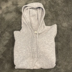 Ljusgrå hoodie i kashmir från Sayless - Mjuk och lyxig ljusgrå hoodie från Sayless i kashmir. Klassisk modell med huva och dragsko, ribbade muddar vid ärmslut och nederkant. Perfekt för en chill och stilren look. Skriv gärna vid frågor// Lorenzo&Co✍️