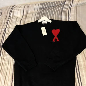 Svart stickad tröja från Ami - Svart stickad tröja från Ami Paris med röd hjärt- och A-detalj på bröstet. Klassisk rund halsringning och långa ärmar. Pris går att diskutera. Ställ frågor!