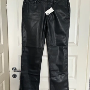 Svarta skinnbyxor från 157 - Snygga svarta skinnbyxor från 157 med klassisk femficksdesign och raka ben. Byxorna har hög midja och stängs med dragkedja och knapp. Perfekta för dig som vill ha en edgy look.