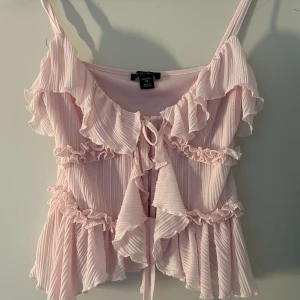 Ljusrosa volangtopp - Supersöt ljusrosa topp med volanger och knyt framtill. Bara använd 1 gång pga fel storlek. 
