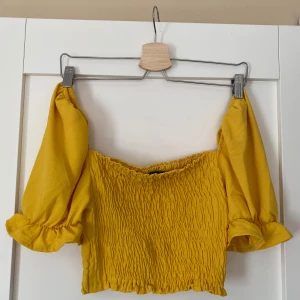 Gul offshoulder topp från Boohoo - Superfin gul offshoulder topp från Boohoo med smockad kropp och puffiga ärmar med volangkant. Croppad modell. I storlek 36. Aldrig använd. 
