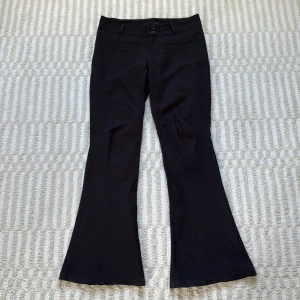Svarta kostymbyxor bootcut - Svarta bootcut kostymbyxor från Gina Tricot i storlek L (passar mig som har M).  Byxorna har medelhög midja, två knappar framtill, bälteshällor och bakfickor med knappar. De är lite slitna nedtill vid fötterna, samt mellan låren