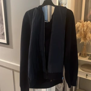 Svart cardigan  från Kappahl - Svart cardigan från Kappahl i storlek M. Cardiganen har huva, långa ärmar och dragkedja framtill. Enkel och stilren design som passar perfekt till chill dagar. Mjuk och skön känsla, perfekt för höst och vinter passar även bra till sommaren. 
