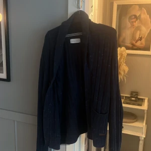 Mörkblå kofta från Pier One - Mysig mörkblå kofta från Pier One med ribbstickat tyg, knappar framtill och två fickor. Snygga bruna mockadetaljer på armbågarna ger en cool touch. Perfekt för lager-på-lager och chill höst- eller vinterstil.