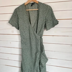 Grön prickig omlottklänning från vero moda - Superfin grön omlottklänning från vero moda med vita prickar. Klänningen har korta ärmar, knyt i midjan och v-ringad hals. Perfekt för dig som gillar en avslappnad men ändå söt stil. Lätt och luftig, passar perfekt till varmare dagar. ☺️💕