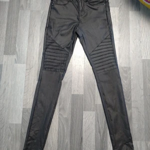 Svarta skinny jeans från ONLY i skinnimitation  - Svarta skinny jeans från ONLY med coola ribbade detaljer över knäna. Byxorna har klassisk femficksdesign och är tillverkade i stretchigt material för en tight passform. Perfekta för dig som gillar en edgy och modern stil.