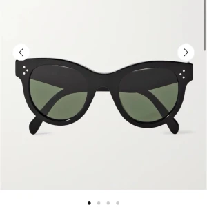 Svarta solglasögon från Céline - Snygga svarta solglasögon från Céline med rundad cat-eye form och gröntonade linser. Bågarna är i blank acetat med ikoniska silverprickar vid fronten. Perfekt accessoar för en cool och stilren look.