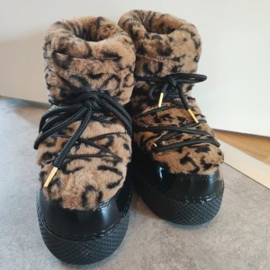 Leopardmönstrade boots från The Happy Fox - Moon boots med leopardmönster från The Happy Fox. Ovandel i mjuk, fluffig pälsimitation och svarta detaljer.