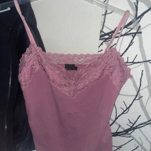 Rosa linnetopp med spets från Stockholm - Supersöt ljusrosa linnetopp från Stockholm med tunna axelband och vacker spets längs v-ringningen. Passar till både jeans och kjol. Storlek M men är mer en S