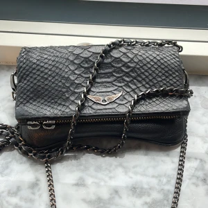 Svart axelväska i skinn med kedja - Säljer min superfina Zadig väska då jag tyvärr inte har någon användning för den längre. Den är i bra skick men saknar två hållare till dragkedjan på framsidan som däremot går att ersätta. Men en bra väska som verkligen går att variera i användningen till olika outfits och ändamål. Pris kan diskuteras!🌸💗