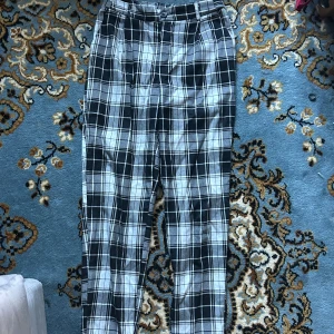 Svarta och vita rutiga kostymbyxor - Snygga kostymbyxor med svartvitt rutigt mönster. Byxorna har normal passform, raka ben och klassisk midja. Perfekta för dig som vill sticka ut lite extra med en stilren look. Materialet känns mjukt och bekvämt, och de har fickor både fram och bak.