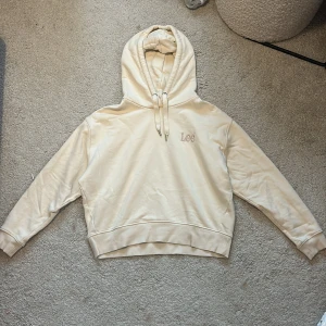 Beige hoodie från Lee med huva - Säljer en beige hoodie från Lee. Tröjan har huva med snörning och broderad Lee-logga på bröstet. Mjuk insida och långa ärmar. Endast använd fåtal gånger och har därför ett väldigt bra skick