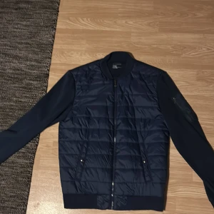Mörkblå bomberjacka Polo Ralph Lauren - Snygg mörkblå bomberjacka från Polo Ralph Lauren med quiltad framsida och släta ärmar. Jackan har dragkedja framtill, ribbade muddar och diskret logga på bröstet. Perfekt för dig som vill ha en stilren och sportig look. Alldeles ny, säljer eftersom den blev för liten.