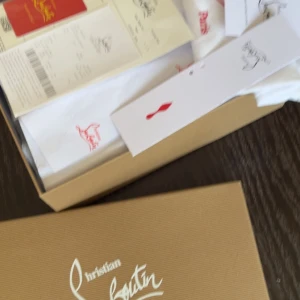 Christian Louboutin svarta sneakers - Svarta sneakers från Christian Louboutin med ikonisk röd sula och snygg snörning. Skorna har rund tå och är tillverkade i mocka och skinn, vilket ger en lyxig känsla. Perfekta för dig som vill sticka ut med exklusiva detaljer och klassisk design.