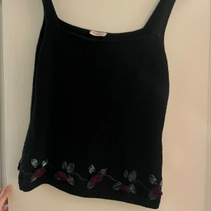 Svart stickad linnetopp från MAX&Co - Unik svart stickad linnetopp i ull från MAX&Co med fina axelband och broderade blommor i vinrött längst ner