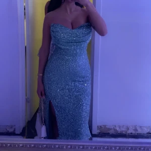 Glittrig grön långklänning - Säljer en superglittrig långklänning i grön med figurnära passform och snygg slits framtill. Klänningen har en draperad, lätt v-ringad överdel. Perfekt för bal eller fest där du vill sticka ut och glänsa. Den har även två armar kan skicka bild om ni vill, Vickte in de i klänningen 