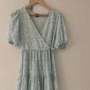 Ljusblå blommig omlottklänning - Supersöt ljusblå kortklänning med vita blommor, puffärmar och omlottmodell med knyt i midjan från Gina tricot.  Bara skriva för fler bilder 💕