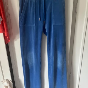 Blå mjukisbyxor i velour - Snygga blå mjukisbyxor i mjuk velour med raka ben, snörning i midjan och stora fickor både fram och bak. Perfekta för chill dagar eller när du vill vara extra bekväm. Fickorna bak har lock med knappar för en cool detalj.