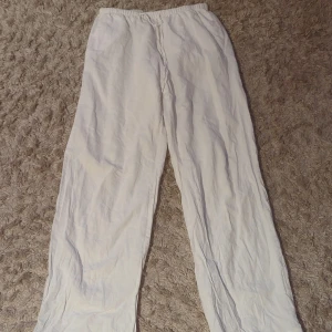 Vita linnebyxor med resårmidja - Säljer ett par vita linnebyxor med avslappnad passform och resår i midjan. Byxorna har raka ben och är perfekta för en chill och luftig stil. Passar lika bra till sneakers som sandaler.