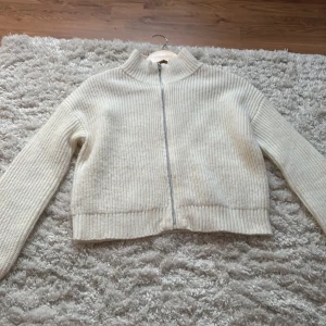 Kräm vit stickad kofta med dragkedja - Mysig vit stickad kofta med hög krage och dragkedja. Materialet är väldigt mjuk och mysigt inte alls sticksigt som vissa andra stickade tröjor kan vara! Tröjan har inga tecken på användning, i princip helt ny!