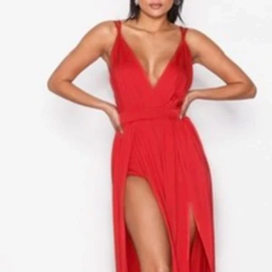 Röd långklänning med slits och v-ringning - Snygg röd långklänning med djup v-ringning och tunna axelband. Klänningen har en insydd body och hög slits framtill med öppen rygg, vilket ger en riktigt cool och elegant look. Perfekt för dig som vill sticka ut och känna dig extra glam