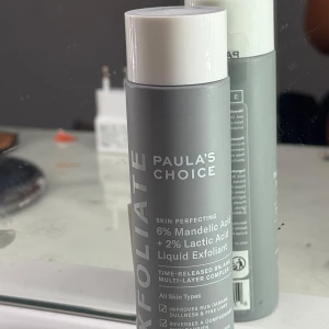 Paula's Choice Liquid Exfoliant - Flytande exfoliering från Paula's Choice med 6% mandelsyra och 2% mjölksyra. Grå flaska med vitt lock, perfekt för att ge huden lyster och jämnare struktur. Passar alla hudtyper och innehåller AHA-syra för effektiv exfoliering.