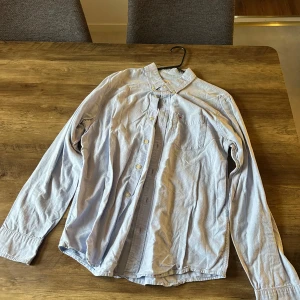 Ljusblå skjorta från Hollister M - Snygg ljusblå skjorta från Hollister i klassisk modell med knappar hela vägen, bröstficka och broderad logga. Skjortan är i bomull och har lång ärm, perfekt för en clean och avslappnad stil.