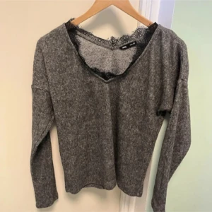 Grå stickad tröja med spetsdetalj - Mysig grå stickad tröja från Gina Tricot med v-ringning och svart spetskant vid halsen. Långärmad och perfekt för lager-på-lager-stil. Enkel att matcha med både jeans och kjol.