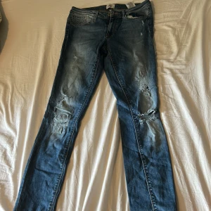Blå slitna skinny jeans från ONLY - Säljer ett par blå skinny jeans från ONLY med slitningar och hål på knäna för en cool, avslappnad look. Jeansen har klassisk femficksdesign, normal passform och är tillverkade i mjukt denimtyg. Perfekta för dig som gillar en trendig streetstyle.
