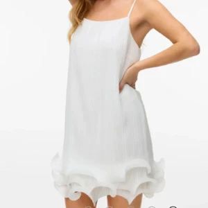 Vit kortklänning med volangkant - Superfin vit kortklänning med tunna axelband och volangdetalj längst ner. Klänningen har en luftig passform och är perfekt för varma dagar. Den är ärmlös och har en lätt, flowy känsla som ger en fräsch och trendig look. Storlek M men passar mig som har S också! Använd 1 gång.