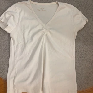 Vit v-ringad t-shirt från Bravo - Vit t-shirt från Bravo Collection med v-ringning och snygg rynkdetalj framtill. Kortärmad modell i mjuk bomull, perfekt för en clean och enkel stil. Passar dig som gillar basic men ändå vill ha något extra.