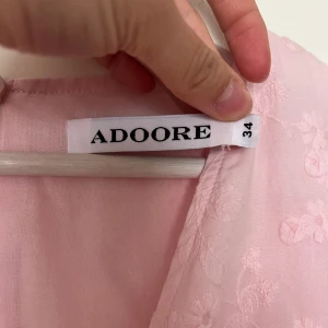 Ljusrosa långklänning från Adoore - Superfin ljusrosa långklänning från Adoore i storlek 34, med broderade blommor, v-ringning och långa puffärmar. Klänningen har knappar framtill och markerad midja för en snygg siluett. Modell Positano dress. 💞  Använd vid två tillfällen, pm för bilder med den på! 