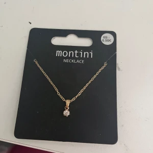 Guldfärgat halsband med sten från Montini - Snyggt och stilrent halsband från Montini med tunn guldfärgad kedja och en liten klar sten som hänge. Perfekt för dig som gillar minimalistiska smycken med en touch av elegans. Kommer på originalförpackning från Ur & Penn.