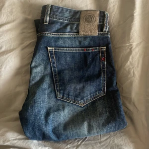 Replay jeans Grover - Snygga Replay jeans i mörkblå med klassiska fem fickor och tydliga kontrastsömmar. Jeansen har raka ben och normal passform, med Replay-logga på bakfickan och läderpatch i midjan. Perfekta för dig som gillar stilrena och tidlösa jeans.