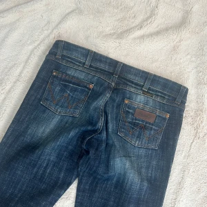 Lågmidjade utsvängda jeans  - Ett par lågmidjade utsvängda jeans från Wrangler i storlek W31 L34. Jeansen är i mycket fint skick (se bilder). Har ingen bild med dom på (för stora) Rakt över midjemått: 41cm. Innebenslängd: 75cm. Total längd: 98cm. Gren: 21cm. Benslut: 21cm. Fast pris. D31