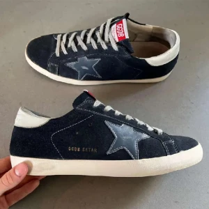 Golden Goose bytes - Snygga svarta sneakers från Golden Goose med grå stjärndetalj på sidan, vit sula och kontrasterande vita detaljer vid häl och snörning. Ovandel i mocka och klassisk låg profil. Perfekta för en cool och avslappnad stil.   Öppen för byten inga köp