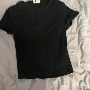 Svart basic t-shirt i bomull - Enkel svart t-shirt med rund hals och korta ärmar. Modellen är klassisk och passar perfekt till jeans eller kjol. Gjord i mjuk bomull för en skön känsla hela dagen. Snygg att bära som den är.