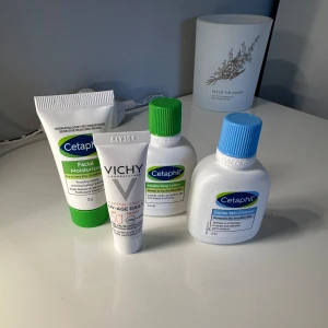 Cetaphil och Vichy hudvårdsprodukter - Fyra hudvårdsprodukter: Cetaphil Facial Moisturizer i tub, Cetaphil Moisturising Lotion och Gentle Skin Cleanser i små flaskor samt Vichy Capital Soleil UV-AGE Daily SPF 50 i vit tub. Perfekt för känslig och torr hud, med återfuktande och rengörande egenskaper.