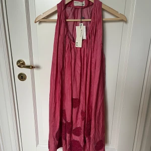 Rosa ärmlös klänning från Rützou - Supersöt rosa kortklänning från Rützou i luftig bomull. Klänningen är ärmlös med avslappnad passform och har stora dekorativa prickar nertill. Perfekt för dig som gillar en lekfull och unik stil.