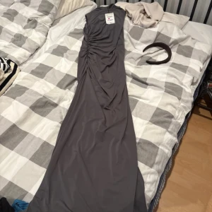 Mörkgrå långklänning från Zara XS - Supersnygg långklänning från Zara i mörkgrått med draperad effekt längs sidan och diskret dragkedja bak. Ärmlös och figurnära passform som ger en clean och modern look. Perfekt för dig som gillar stilrena vibes och vill sticka ut på nästa event.