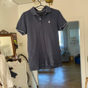 Pikétröja  - Snygg mörkblå pikétröja från Sail Racing i bomull. Klassisk krage med två knappar och vit piping på ärmslut och krage. Liten broderad logga på bröstet och nacken. Perfekt för en clean och sportig look. Stlk XS