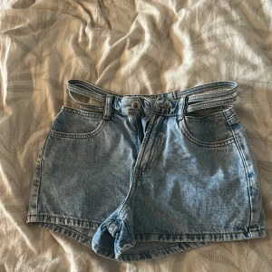 Unika jeansshorts med strassbälte - Säljer ett par ljusblå högmidjade jeansshorts från Monki med ett riktigt coolt dubbelt bälte i midjan dekorerat med strass. Klassisk femficksmodell och snygg tvättad denim. Perfekta för dig som vill sticka ut lite extra i sommar!