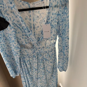 Blommig långklänning från Vila - Superfin långklänning från Vila i vitt och ljusblått blommönster. Klänningen har v-ringning, långärmade ärmar. Perfekt för sommarens alla tillfällen!