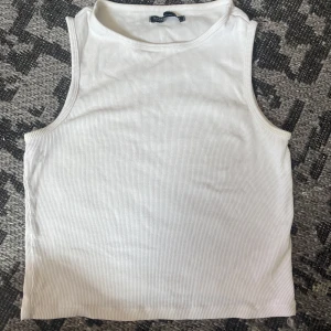 Vit ribbad topp från House - Säljer en fräsch vit ribbad topp från House i ekologisk bomull. Toppen är ärmlös med klassisk rund halsringning och har en clean, enkel look som passar till allt. Perfekt för varma dagar eller som lager under skjorta.