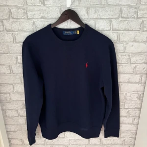 Ralph Lauren tröja - Enkel och stilren tröja från Ralph Lauren med röd logga på bröstet. Sitter snyggt och passar till det mesta. I bra skick och bara använd sparsamt – redo för ny ägare! Hör av dig vid intresse 🙌