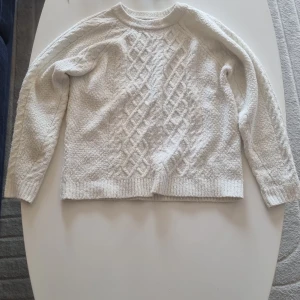 Vit stickad tröja från 157 - Mysig vit stickad tröja från 157 med snyggt kabelstickat mönster framtill och ribbade muddar. Perfekt för kyliga dagar och passar till allt. Klassisk rund halsringning och långärmad modell.