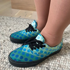 Vans Oddity Space blåprickiga sneakers - Unika Vans sneakers från David Bowie kollektionen med blå och turkosa prickar på ljusgrön bas. Svarta snören och sula med texten 'ODDITY' och 'SPACE' på sidorna. Klassisk låg modell i textil, perfekt för dig som gillar färg och mönster.