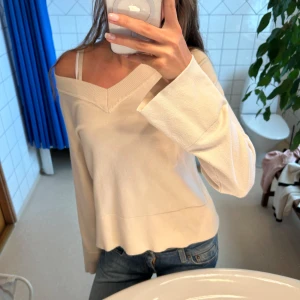 Vit offshoulder tröja med v-ringning - Säljer en stilren vit tröja med bred v-ringning och offshoulder-design. Tröjan har långa, vida ärmar och är tillverkad i ett mjukt material som känns skönt mot huden. Perfekt för dig som gillar en avslappnad men trendig look.
